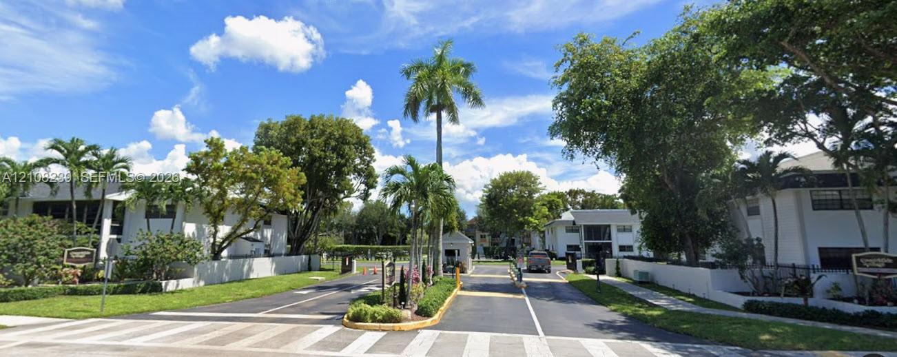 Gated entry featuring a controlled access system, paved multi-lane driveway, mature palm trees, and manicured landscaping