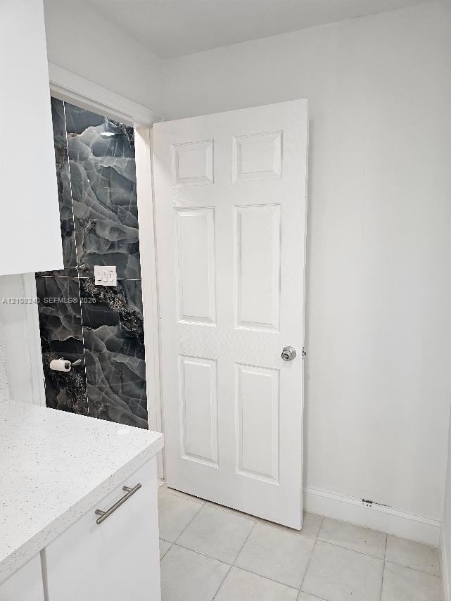 Six-panel interior door with a polished metal knob, white cabinetry featuring a light-toned countertop, and dark-toned stone-finish tile wall accent