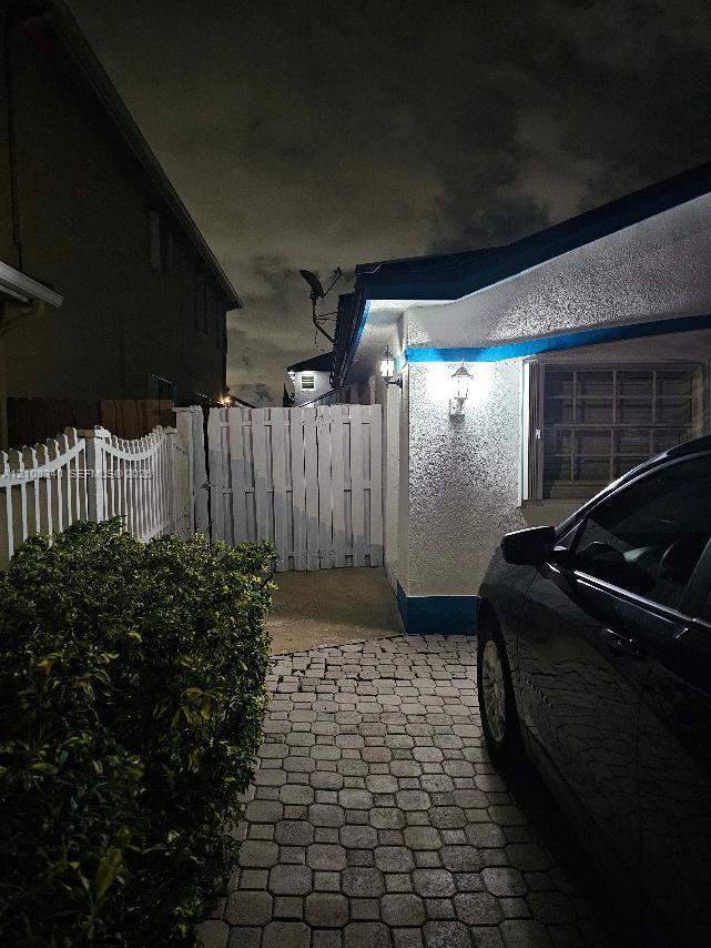 Textured stucco exterior featuring stone paver driveway, white privacy fencing, and exterior wall-mounted light fixtures