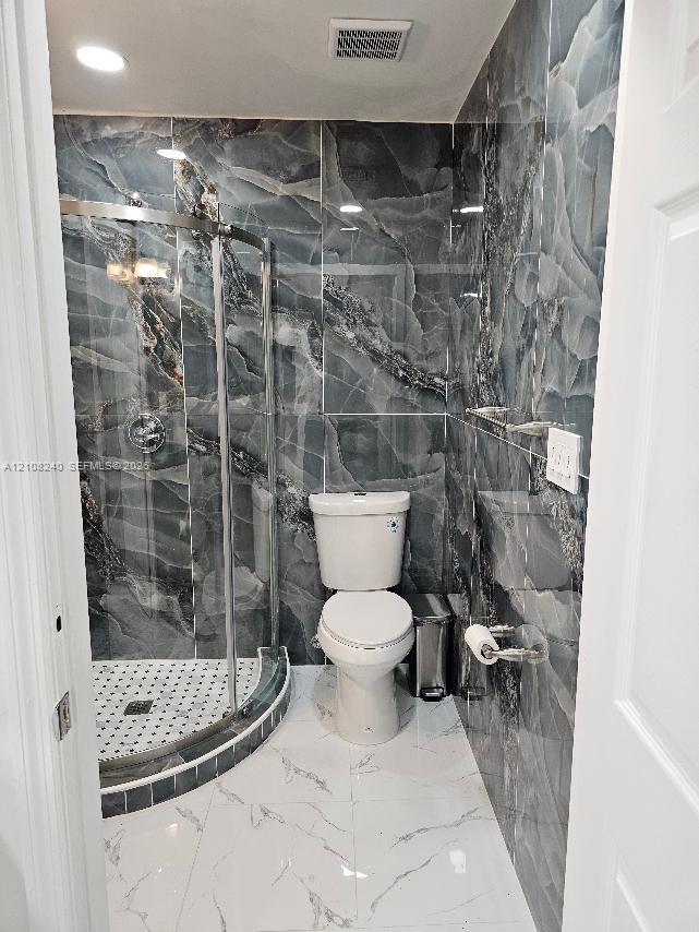 Bathroom featuring floor-to-ceiling dark-veined wall tile, a corner glass-enclosed shower with a mosaic-tile basin, and large-format white tile flooring with veining detail