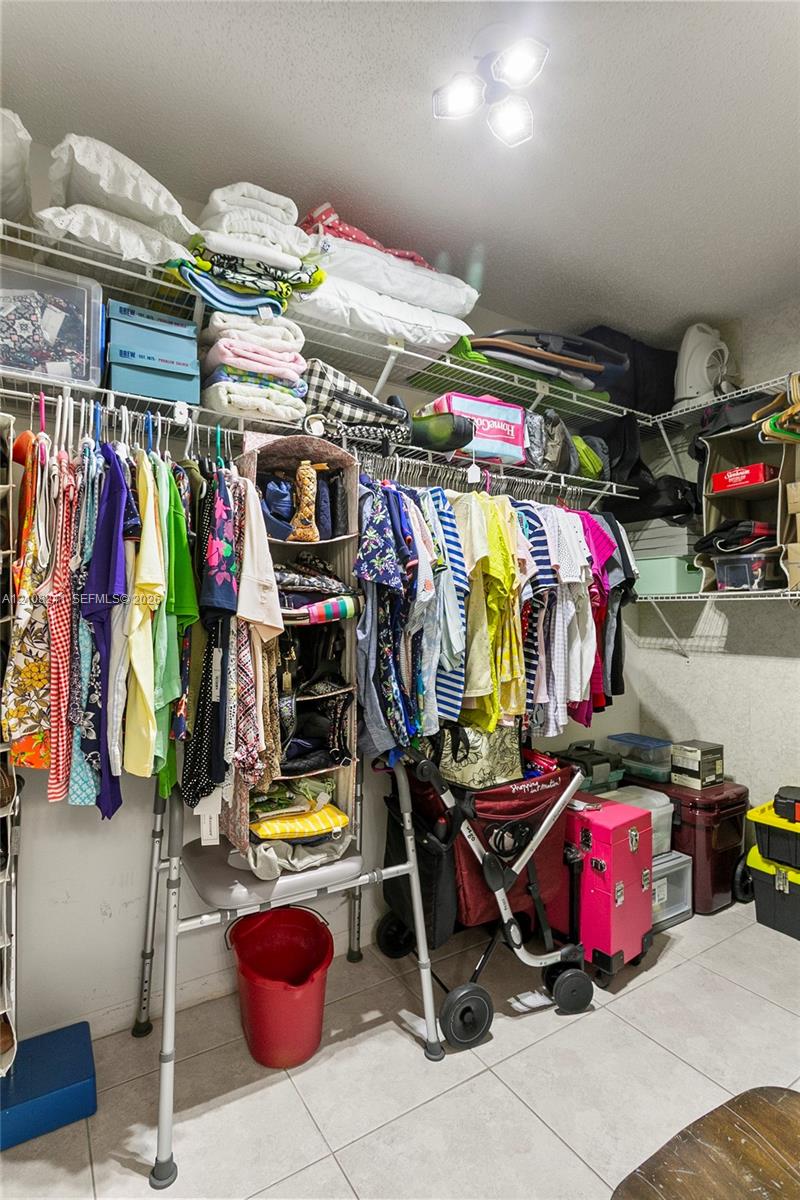Walk-in closet featuring wire shelving, triple-tiered storage racks, tile flooring, and flush-mount overhead lighting Walk-in closet featuring wire shelving, triple-tiered storage racks, tile flooring, and flush-mount overhead lighting
