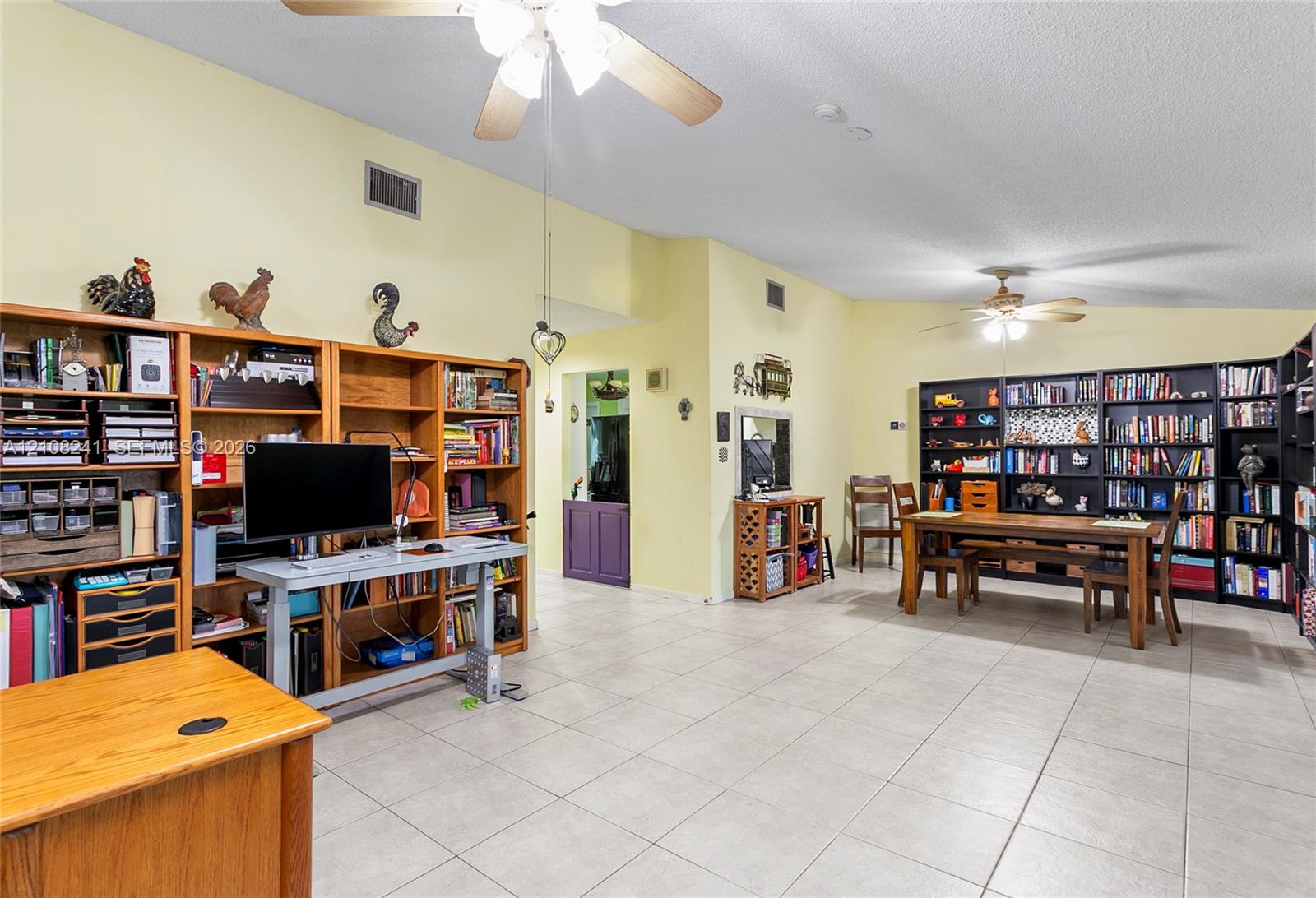 Vaulted ceilings, neutral tile flooring, dual ceiling fans, and extensive built-in wooden shelving units