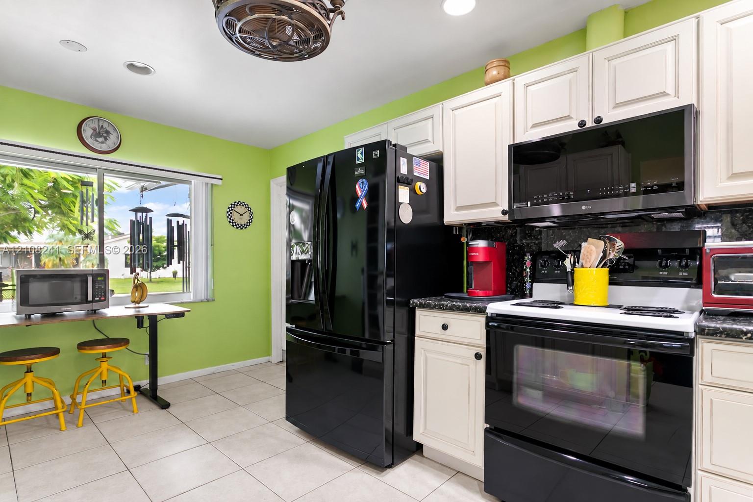 Kitchen featuring off-white cabinetry, black appliances, dark stone-finish countertops, tile flooring, and a large window Kitchen featuring off-white cabinetry, black appliances, dark stone-finish countertops, tile flooring, and a large window