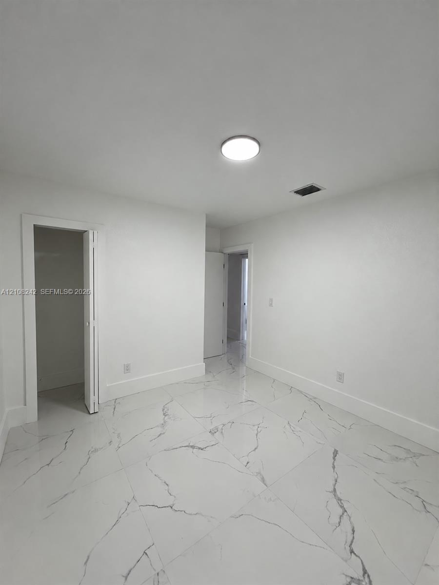 Neutral-toned interior space featuring large-format white stone-finish tile flooring with grey veining, a flush-mount circular ceiling light, and a built-in closet with bi-fold doors