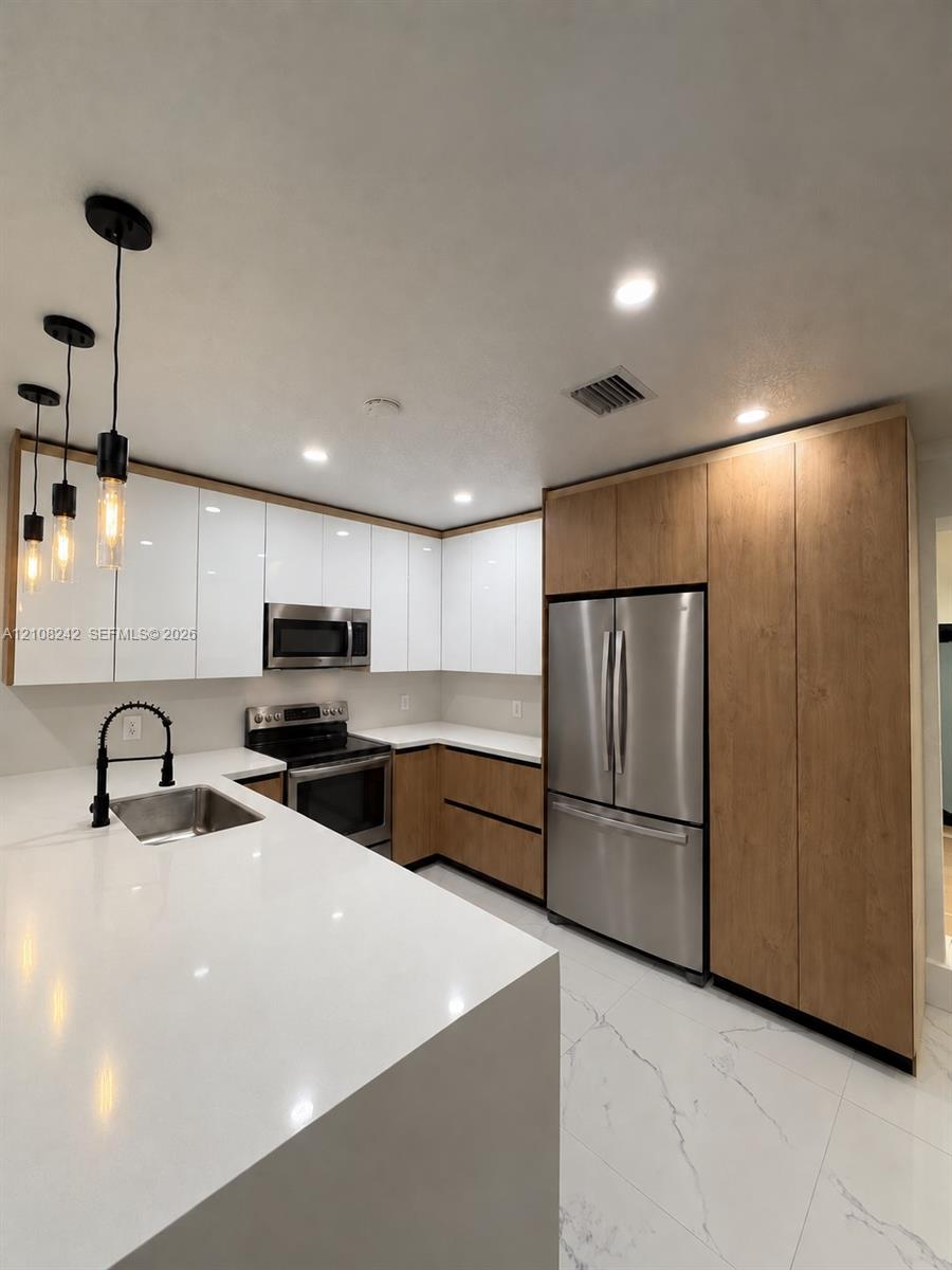 Kitchen featuring white gloss cabinetry, wood-finish lower cabinets, quartz countertops, stainless steel appliances, and matte black pendant lighting