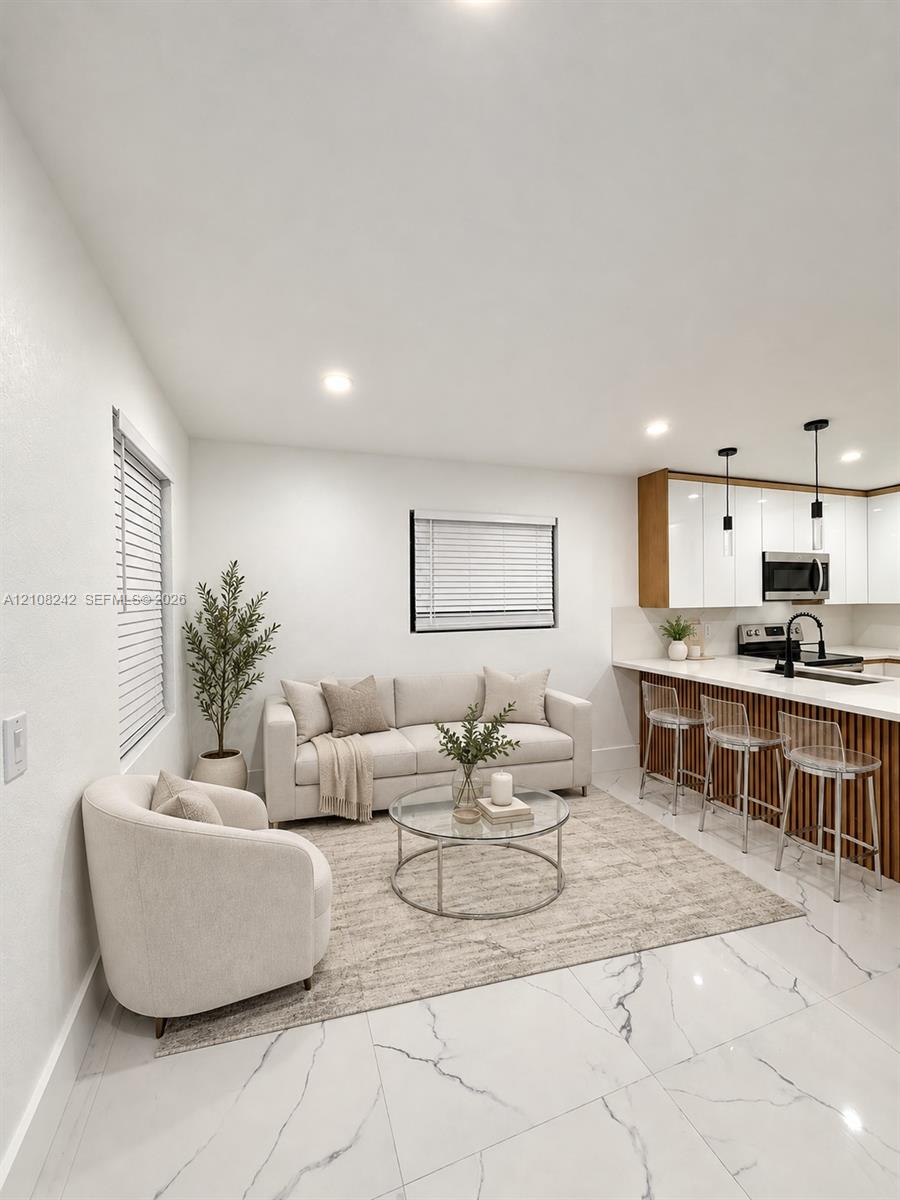 Kitchen area featuring white gloss cabinetry, vertical wood-slat island paneling, stone-finish countertops, recessed lighting, and large-format tile flooring