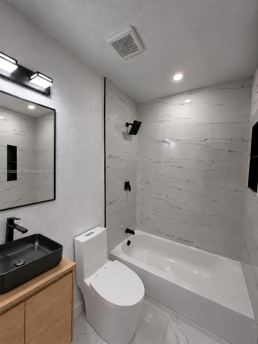 Bathroom featuring a wood-finish vanity, matte black fixtures, rectangular vessel sink, and full-height wall tile surrounding the bathtub