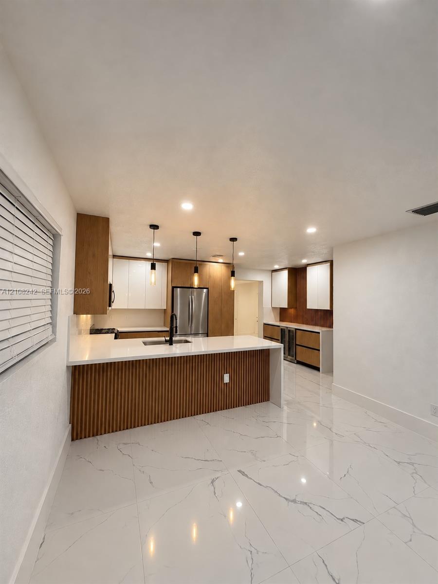 Kitchen featuring custom two-tone cabinetry with slatted wood detailing, white stone countertops, large-format veined porcelain tile flooring, stainless steel built-in appliances, and pendant lighting