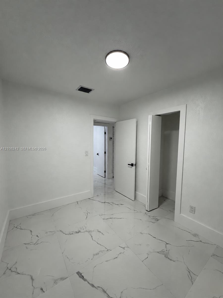 Large-format stone-style tile flooring with veining, solid-core interior doors, matte black hardware, and a flush-mount LED ceiling fixture