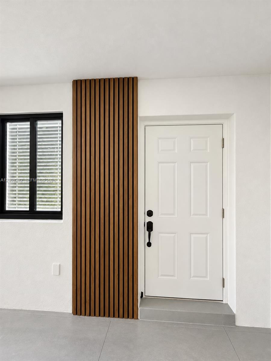 Vertical wood-slat accent wall, six-panel entry door with matte black hardware, black-framed window, and neutral large-format floor tiling