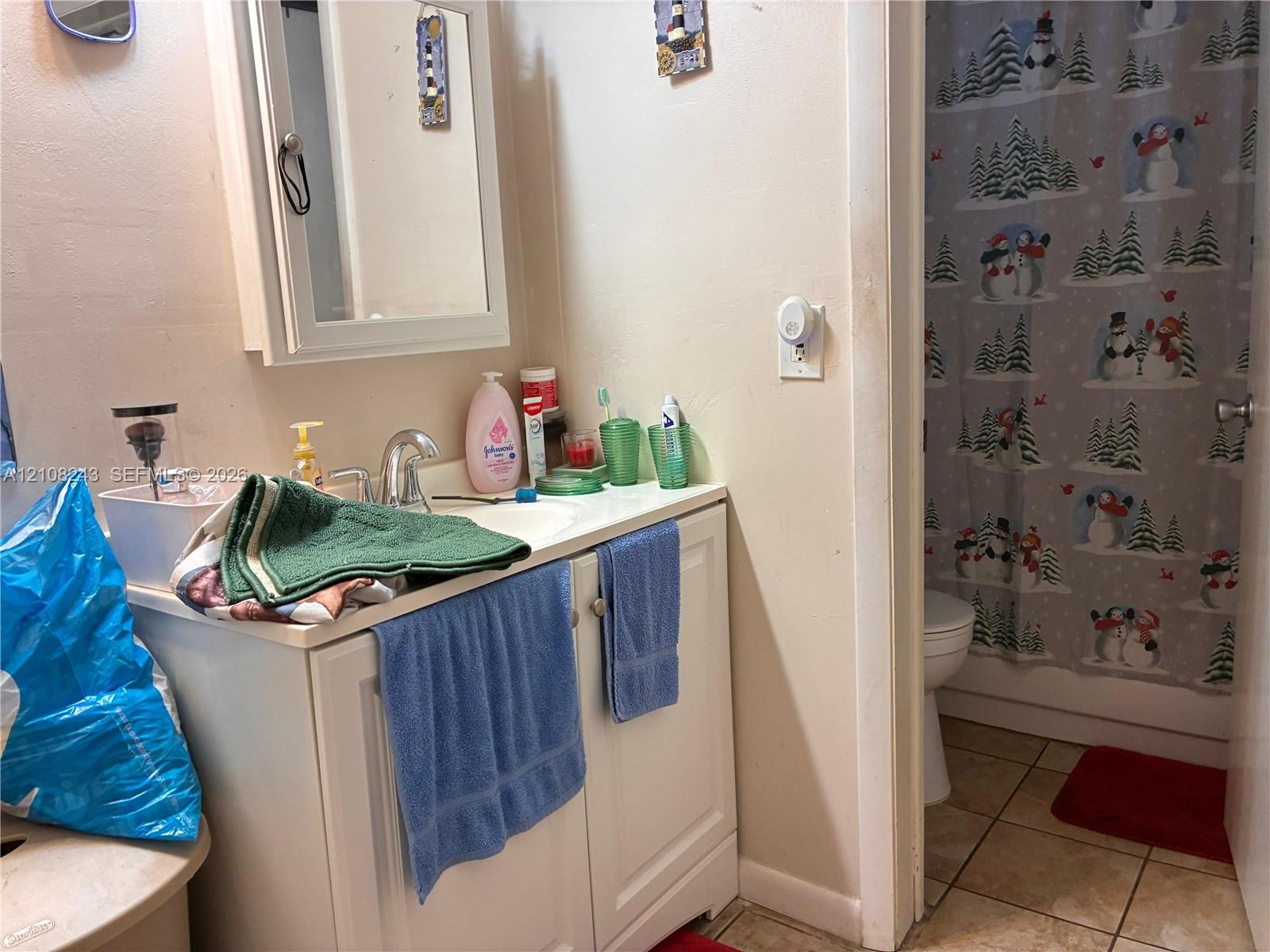 Bathroom featuring a white vanity cabinet with an integrated sink, a wall-mounted mirrored medicine cabinet, and tile flooring