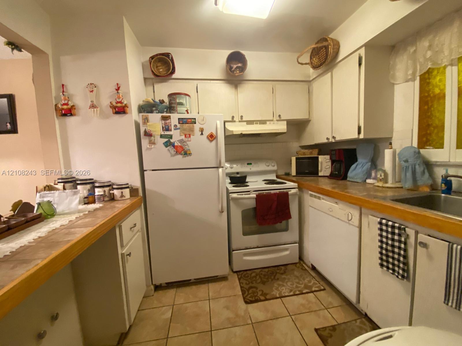 Kitchen featuring white cabinetry, solid-surface countertops, tile flooring, built-in range, and a drop-in stainless steel sink