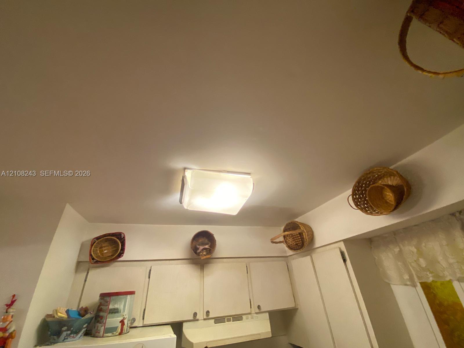 Square flush-mount ceiling light fixture with an opaque glass shade, paired with white solid-panel upper cabinetry and a matching range hood