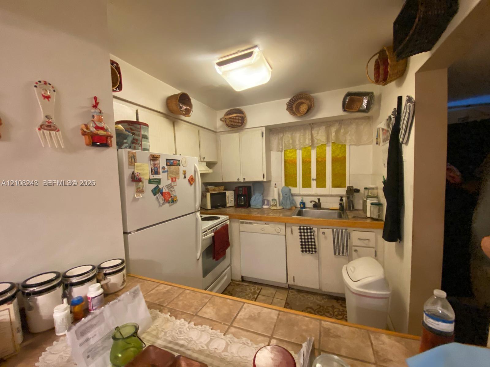 Kitchen featuring white cabinetry, tile-topped peninsula, integrated dishwasher, and multi-pane window
