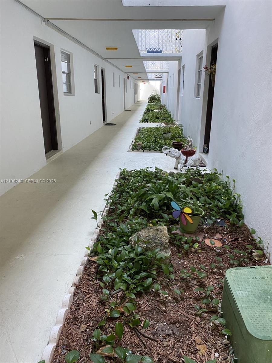 Open-air corridor featuring painted masonry walls, recessed lighting, and integrated landscape beds with scalloped stone edging