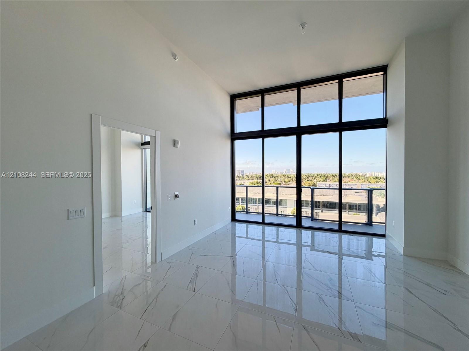 High-ceiling living area featuring large-format polished stone-finish flooring, floor-to-ceiling windows with dark framing, and a private balcony High-ceiling living area featuring large-format polished stone-finish flooring, floor-to-ceiling windows with dark framing, and a private balcony