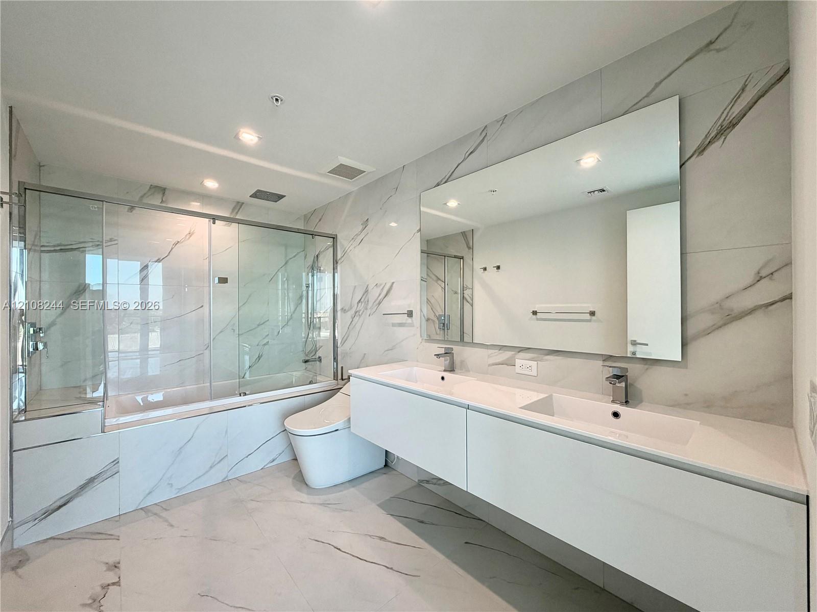 High-ceiling interior featuring stone-finish tile flooring with veining detail, recessed lighting, and white louvered-panel closet doors High-ceiling interior featuring stone-finish tile flooring with veining detail, recessed lighting, and white louvered-panel closet doors
