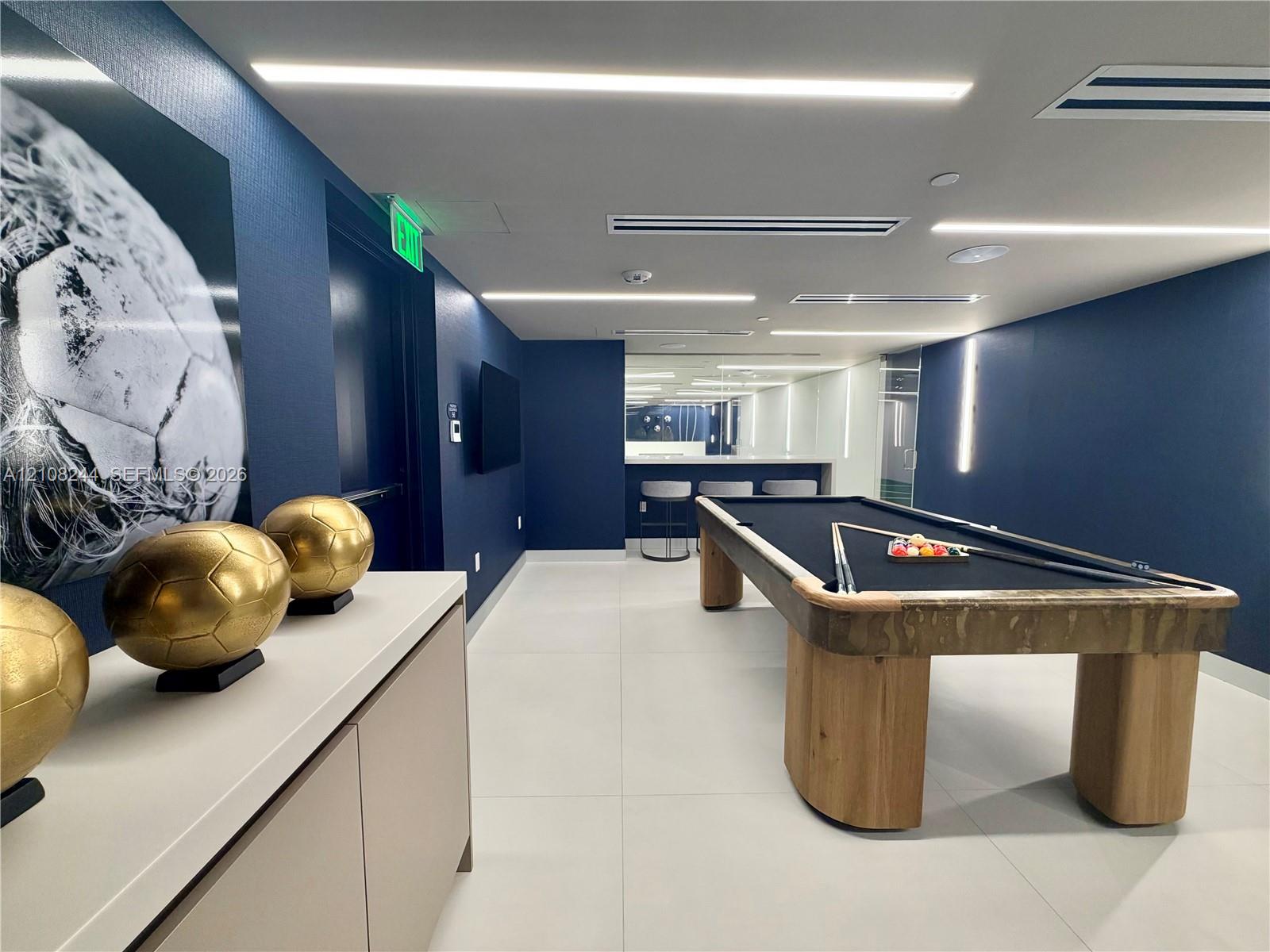 Recreation room featuring integrated projector equipment, a specialized synthetic turf flooring area, high-contrast ceiling paint, and minimalist vertical accent lighting