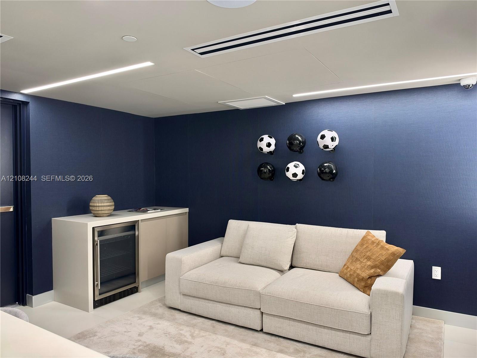 Recreation room featuring large-format tile flooring, recessed linear lighting, navy-toned walls, and a built-in refreshment counter