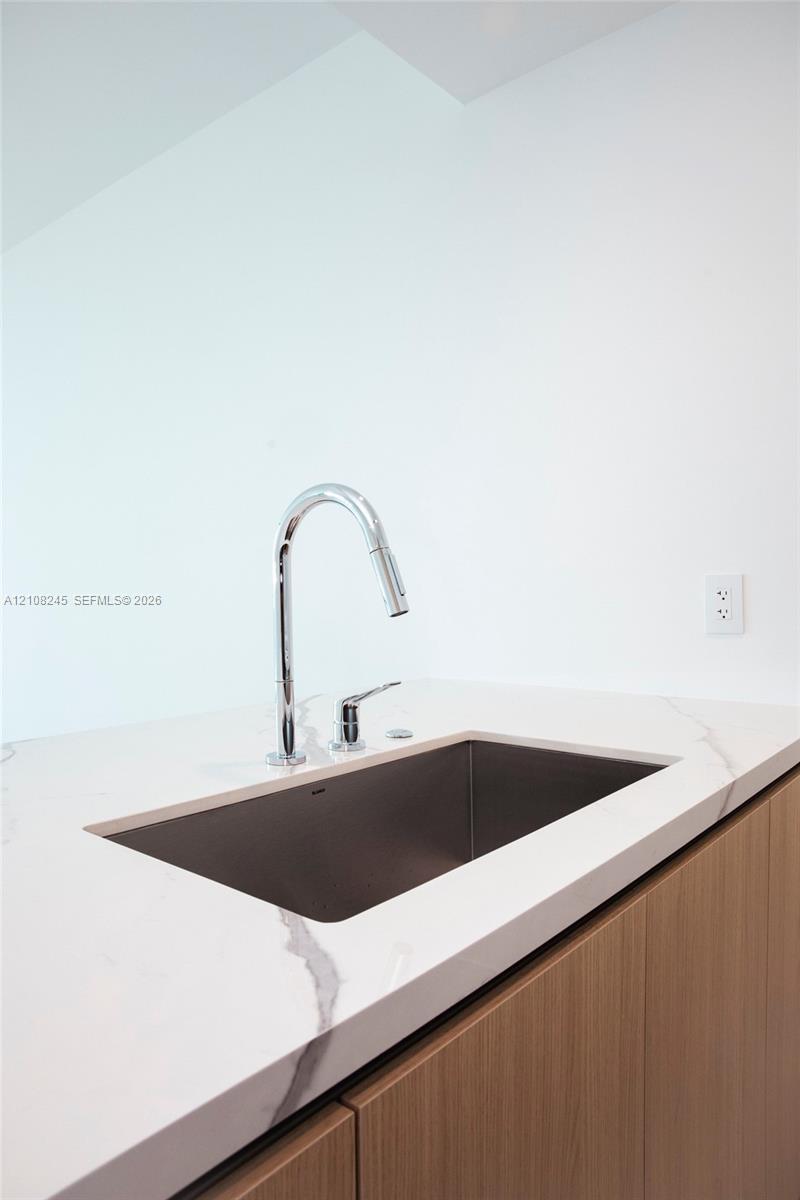 Undermount stainless steel kitchen sink with a high-arch chrome pull-down faucet, stone-finish countertop with veining, and flat-panel wood-finish cabinetry