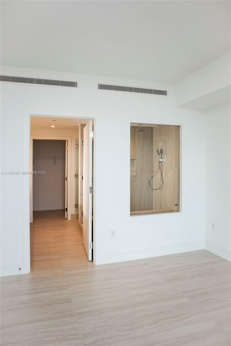 Wood-finish flooring, glass-enclosed shower stall with neutral tile surround, and recessed ceiling lighting