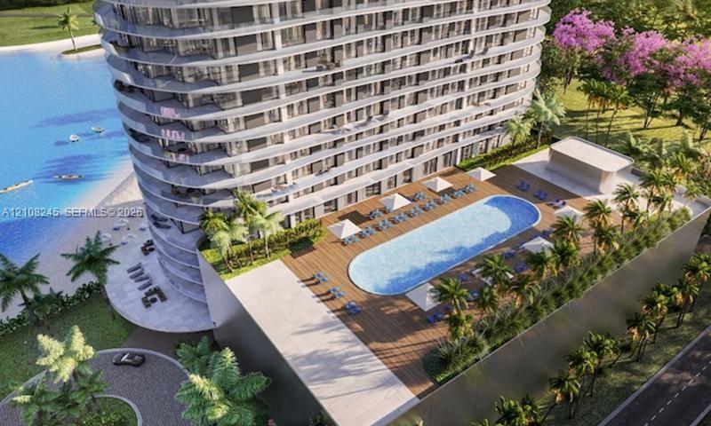 High-rise residential building featuring curved balconies, an elevated swimming pool with wood-finish decking, and landscaped grounds with mature palm trees