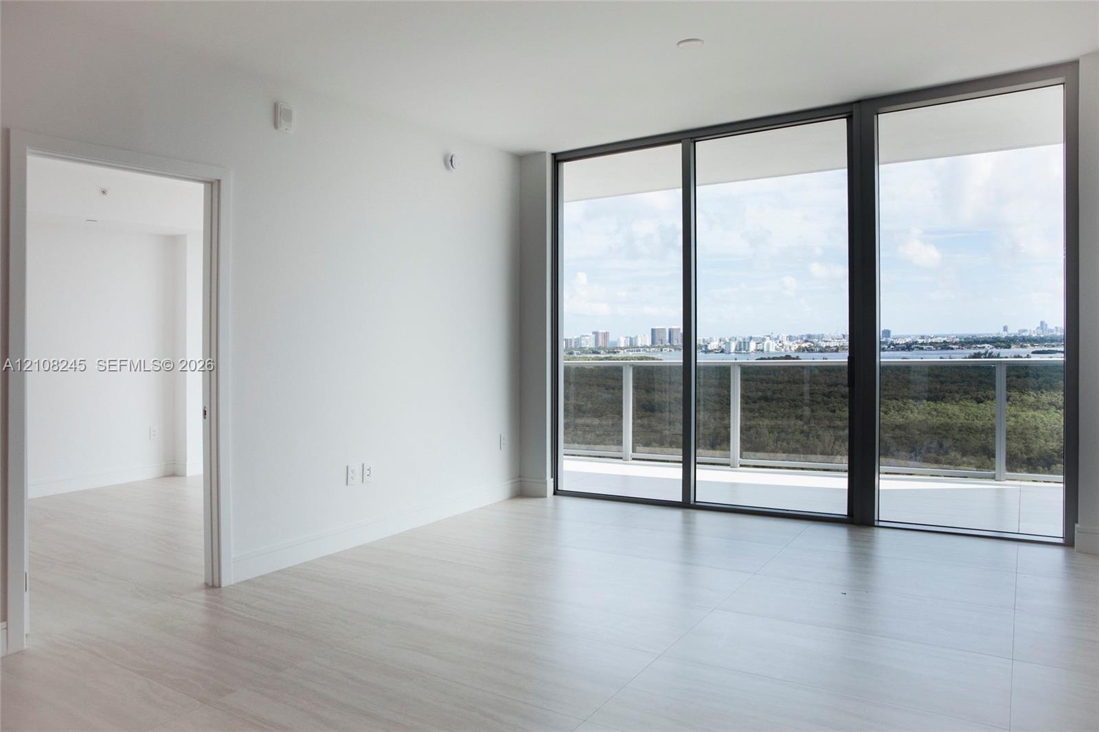 Floor-to-ceiling glass panel windows, light-toned tile flooring, and an integrated outdoor balcony with a metal railing