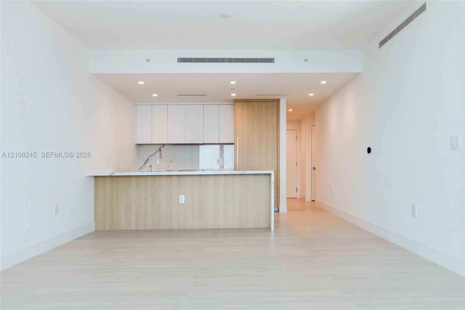 Kitchen featuring flat-panel cabinetry, light-toned wood-finish panels, stone-surface countertops, recessed ceiling lighting, and wood-finish flooring