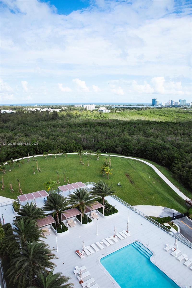 Pool deck featuring a swimming pool, multiple shaded cabanas, mature palm trees, and expansive grassy grounds
