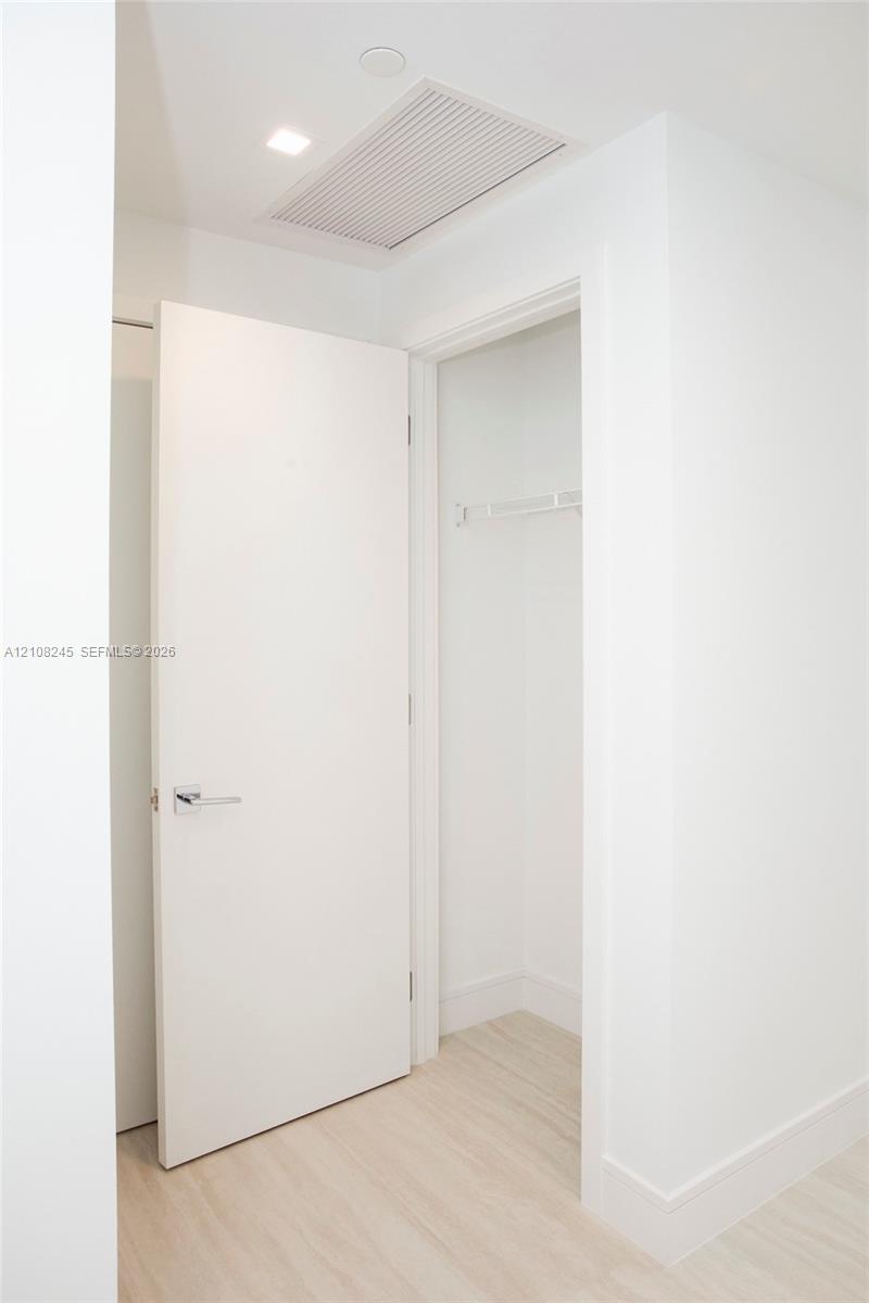 Solid core interior door featuring a satin chrome lever handle, wood-finish flooring, and a built-in closet with integrated shelving