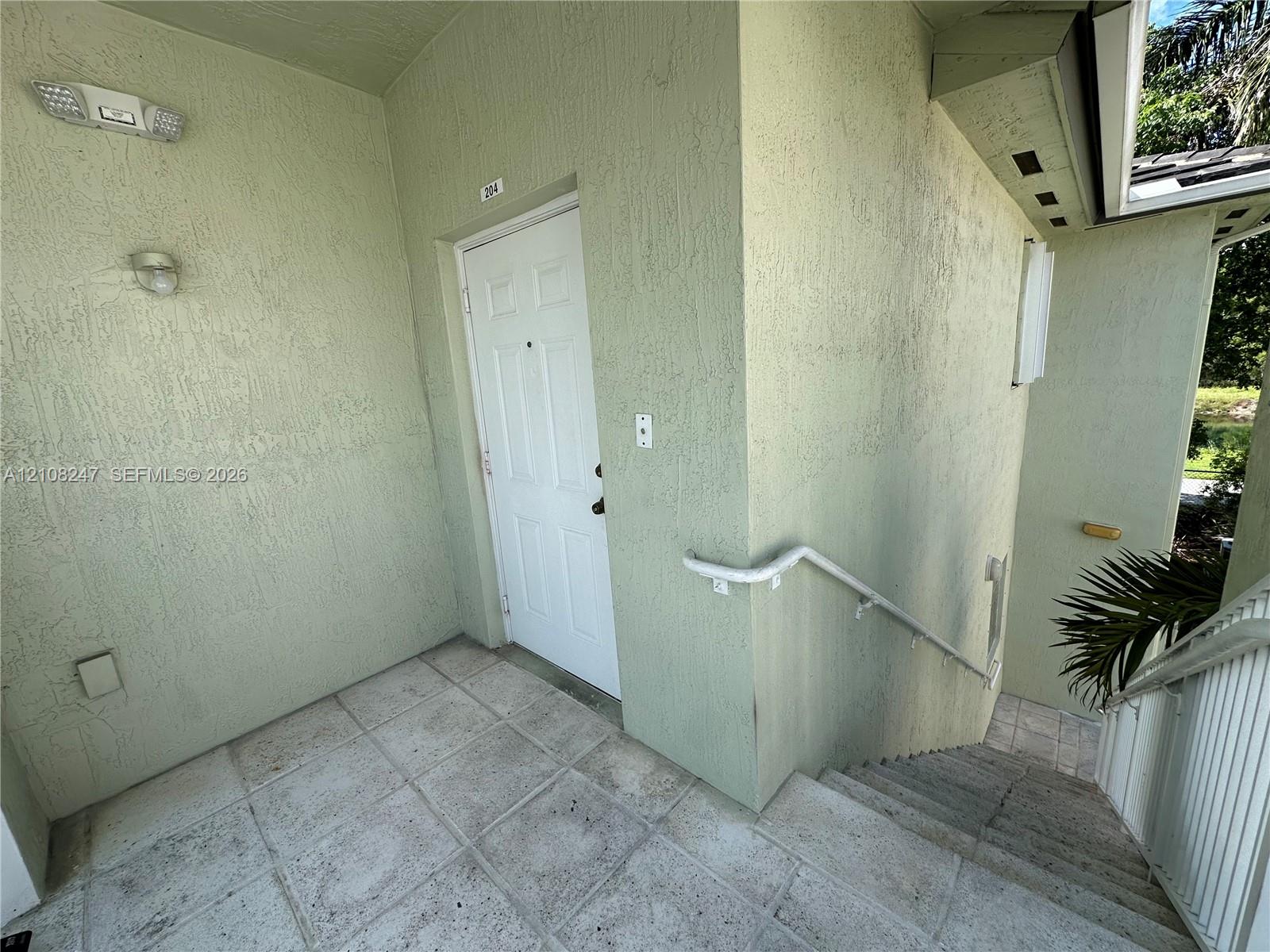 Covered entryway featuring textured stucco exterior walls, tiled flooring, wall-mounted lighting, and a white six-panel entry door