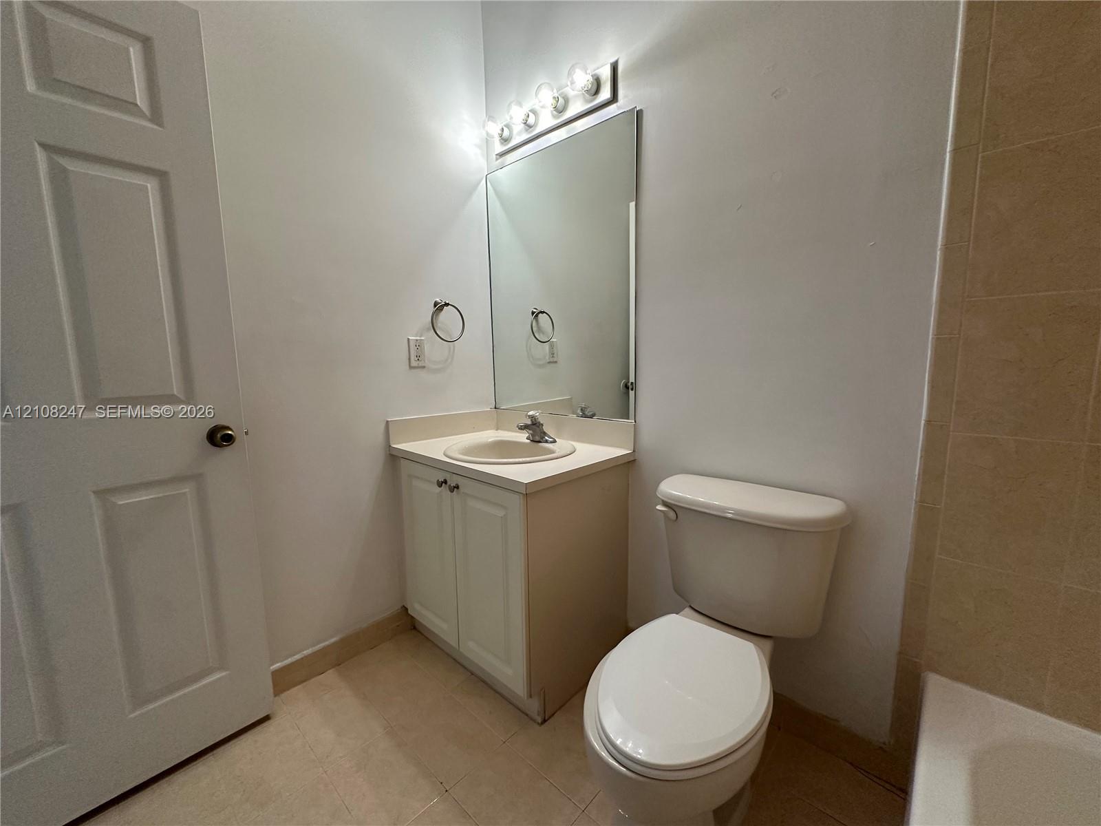 Bathroom featuring a vanity with a recessed basin, a large wall-mounted mirror, a multi-bulb vanity light fixture, and tile flooring
