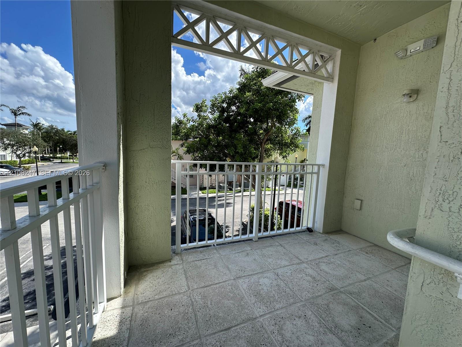 Covered balcony featuring tiled flooring, white metal railings, decorative lattice woodwork, and stucco wall finishes