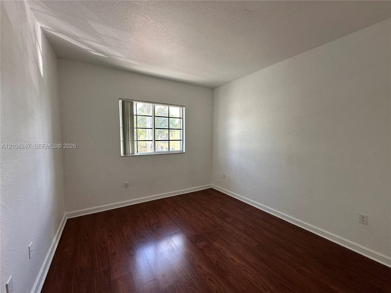 Neutral-toned walls paired with wood-finish flooring and a multi-pane window featuring vertical blinds