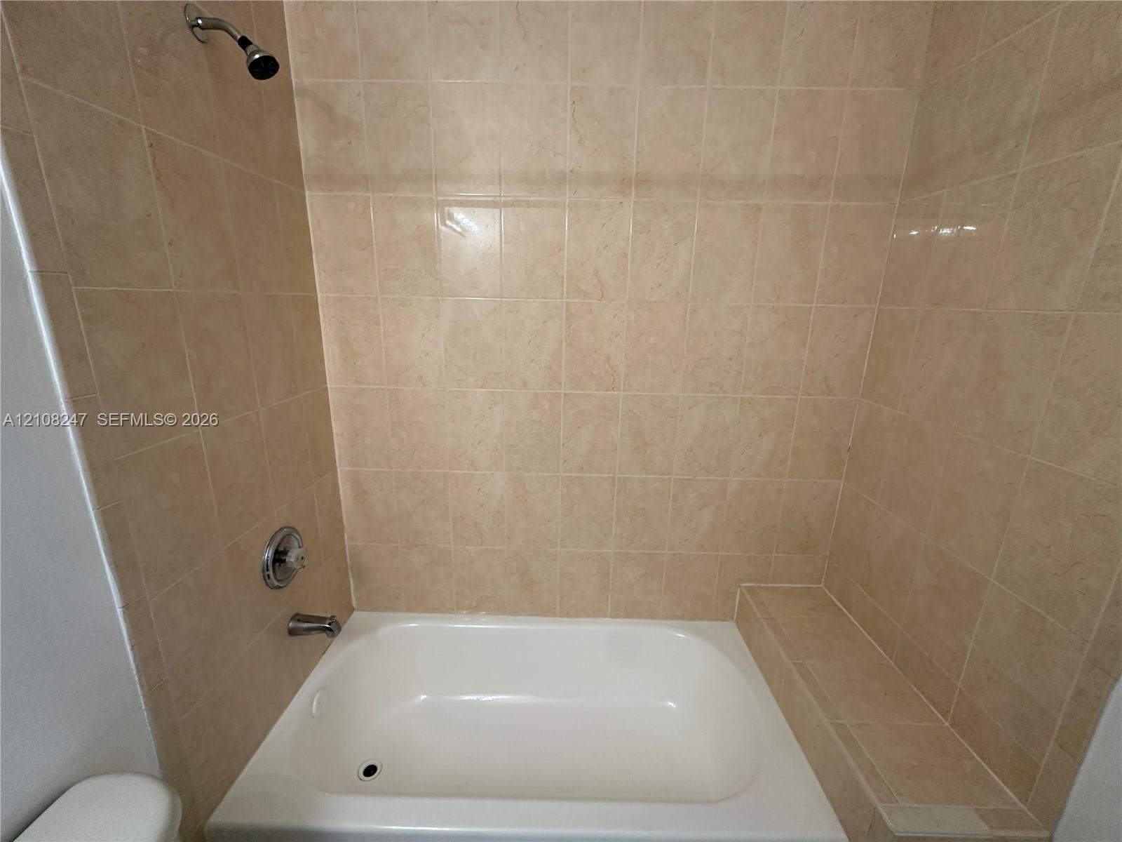Bathtub featuring a built-in tiled ledge, neutral wall-to-wall ceramic tile surround, and metallic shower hardware