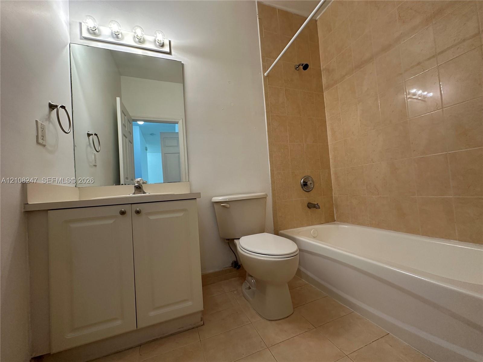 Bathroom featuring a vanity cabinet with a countertop basin, a wall-mounted mirror with a four-light fixture, and a tub with tiled surround