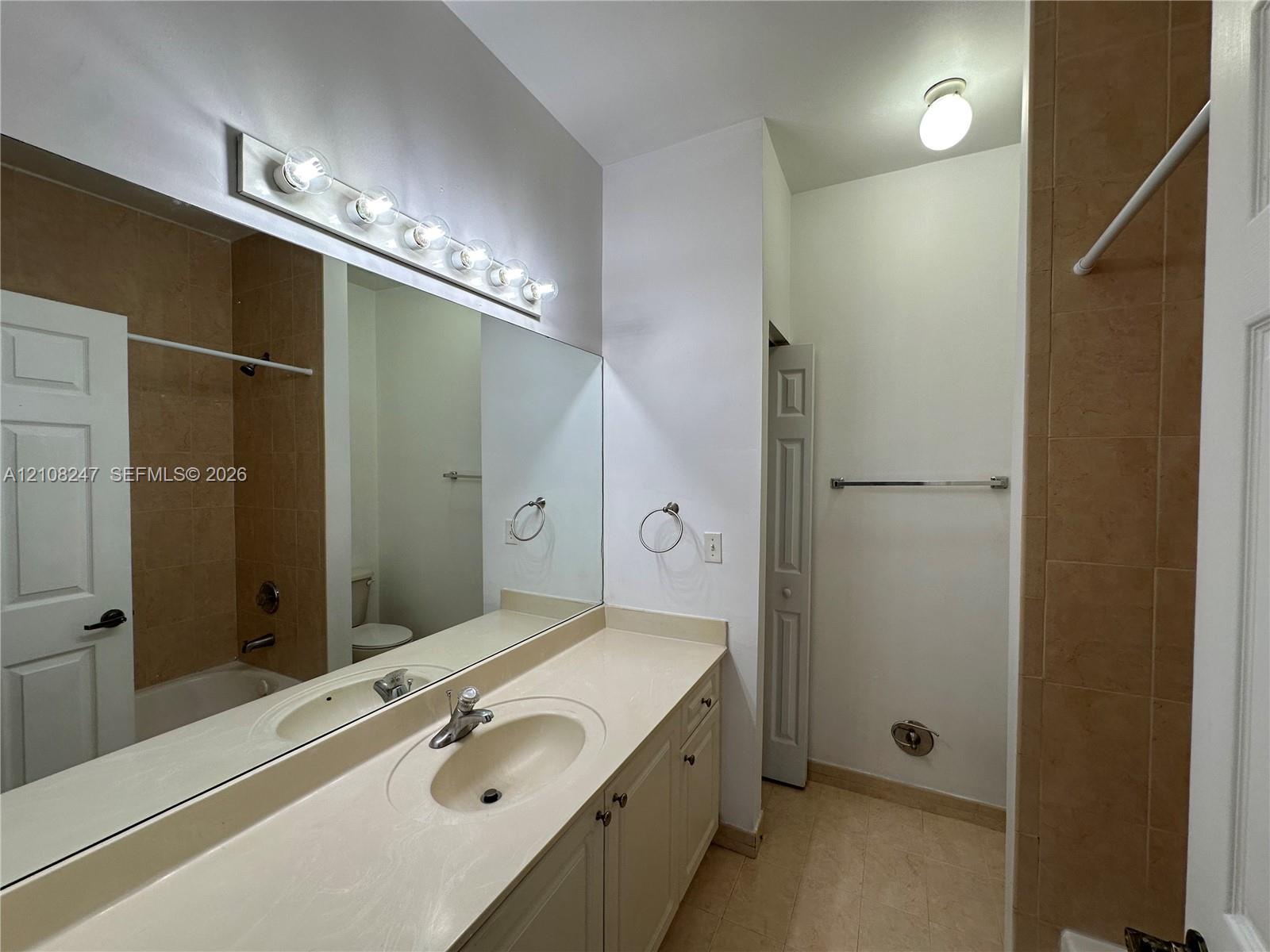 Bathroom featuring a neutral vanity with an integrated sink, a full-width vanity mirror, a six-bulb wall-mounted light fixture, and tile-surround tub area