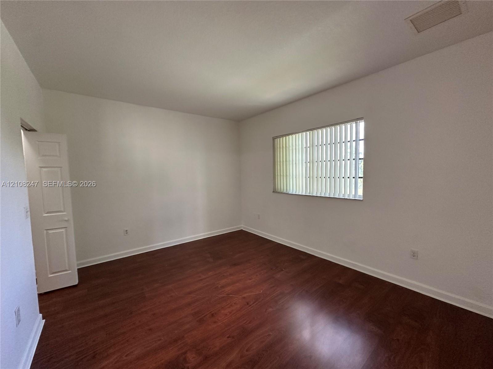 Interior room featuring wood-finish flooring, a single-panel interior door, and a horizontal window with vertical blinds