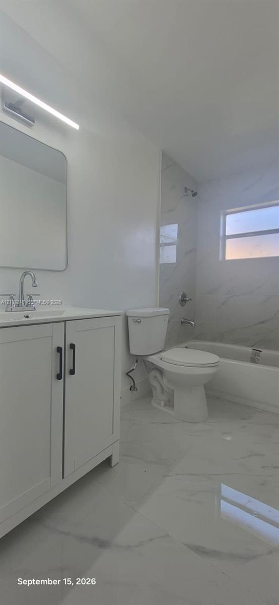 Bathroom featuring a white vanity cabinet with matte black hardware, stone-finish tile flooring, tub-shower combination with floor-to-ceiling tile surround, and an integrated LED vanity light