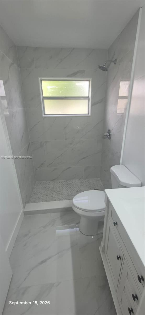 Walk-in shower featuring floor-to-ceiling stone-pattern tile, mosaic tile flooring, a window, and a built-in vanity with a solid-surface countertop