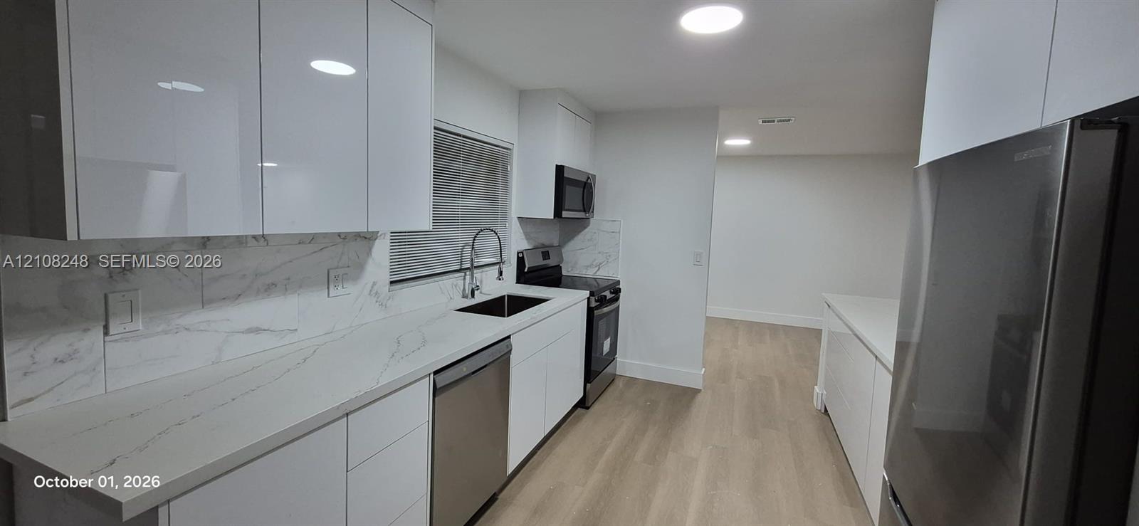 Kitchen featuring high-gloss white cabinetry, stone-finish countertops with matching backsplash, stainless steel appliances, and wood-finish flooring