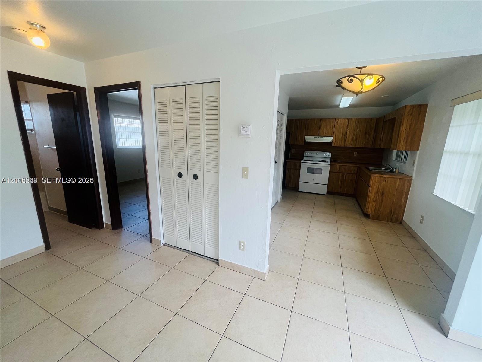 Kitchen featuring wood-finish cabinetry, tile flooring, and overhead lighting, complemented by a hallway with louvered-panel closet doors and dark-finish interior door frames