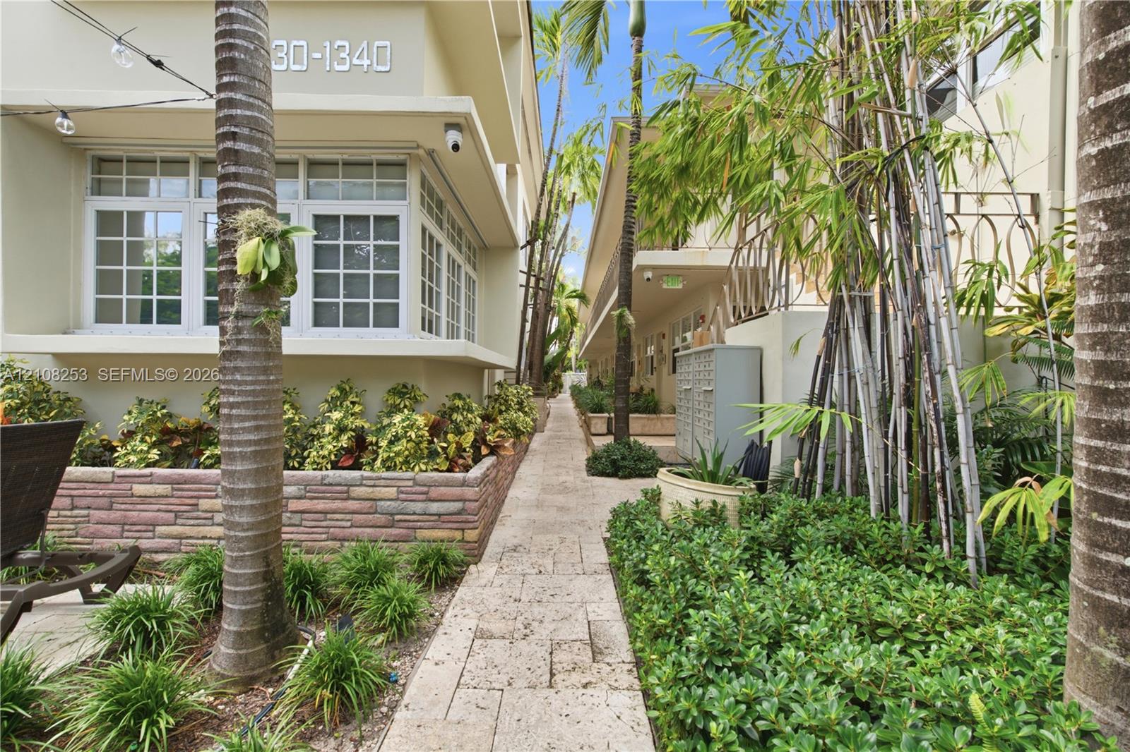 Exterior walkway featuring stone paver flooring, tiered stone-finish planters, multi-pane windows, and lush tropical landscaping Exterior walkway featuring stone paver flooring, tiered stone-finish planters, multi-pane windows, and lush tropical landscaping
