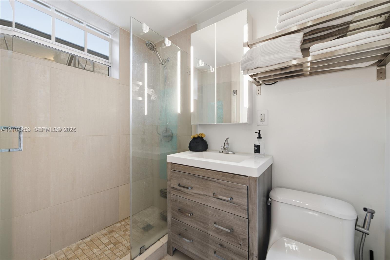 Walk-in shower featuring floor-to-ceiling tile, frameless glass enclosure, and a handheld shower head