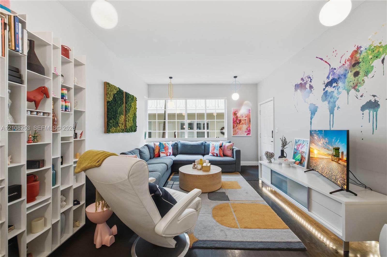 Floor-to-ceiling white built-in shelving, multi-pane window, integrated low-profile media cabinetry with under-cabinet lighting, and dark-finish flooring