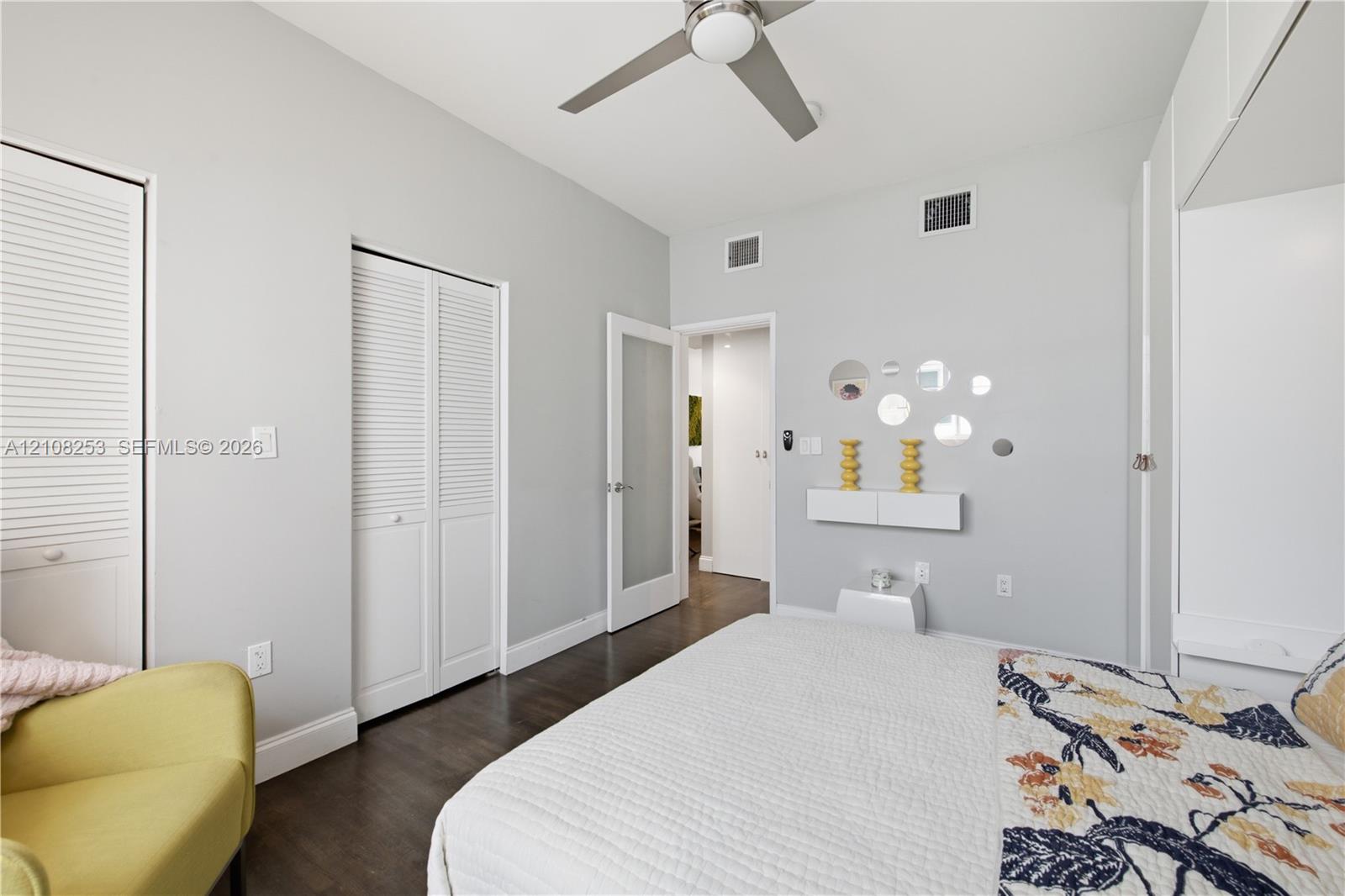 Wood-finish flooring, white louvered closet doors, modern ceiling fan with integrated lighting, and a white interior door with a frosted glass pane
