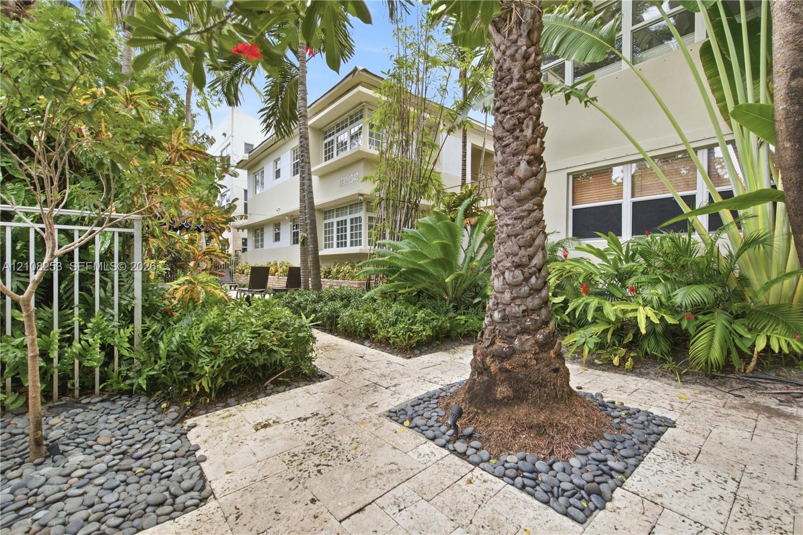 Landscaped courtyard featuring stone paver walkways, decorative pebble borders, mature palm trees, and lush tropical greenery