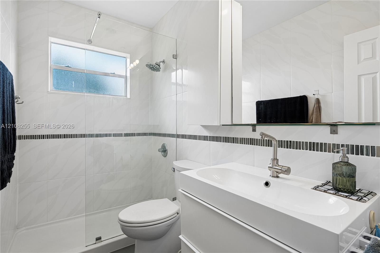 Bathroom featuring white wall tile with a mosaic accent border, a glass-enclosed shower, a floating vanity with an integrated sink, and brushed-nickel hardware