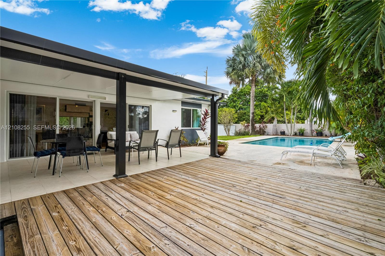 Covered patio featuring a wood-plank deck, tile flooring, sliding glass doors, and a swimming pool with a stone pool deck