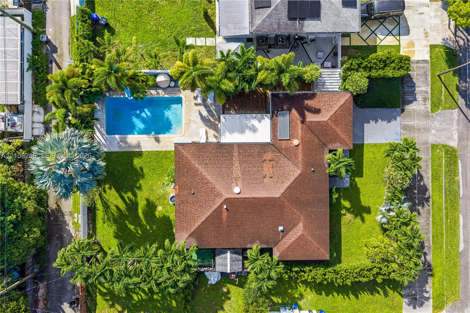 Aerial perspective featuring a shingled roof, an inground swimming pool, paved patio areas, and manicured landscaping with mature palm trees